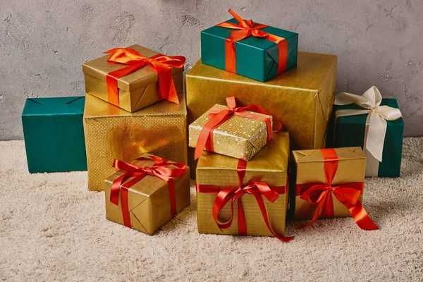 Caixas de presente de Natal turquesa e dourada com fitas vermelhas no tapete no quarto — Fotografia de Stock