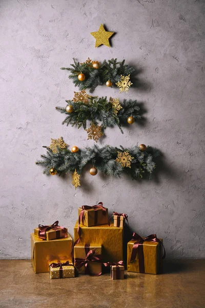 Árbol de Navidad hecho a mano de ramitas colgadas en la pared gris, cajas de regalo en el suelo en la habitación - foto de stock