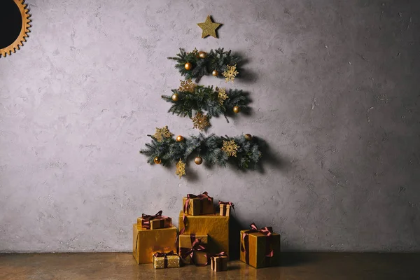 Árbol de Navidad hecho a mano colgando en la pared gris, cajas de regalo en el piso en la habitación - foto de stock
