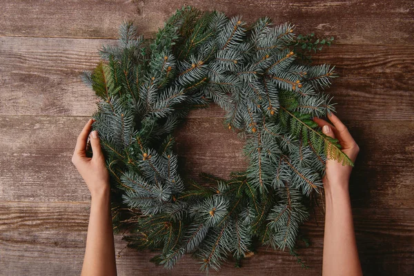 Cropped image of woman holding christmas fir wreath at wooden table — Stock Photo