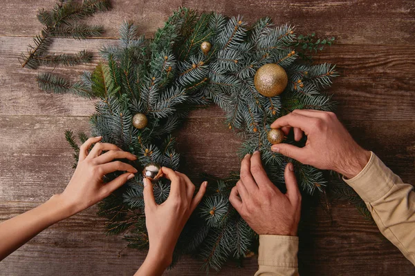 Imagen recortada de pareja decorando la corona de abeto de Navidad juntos - foto de stock