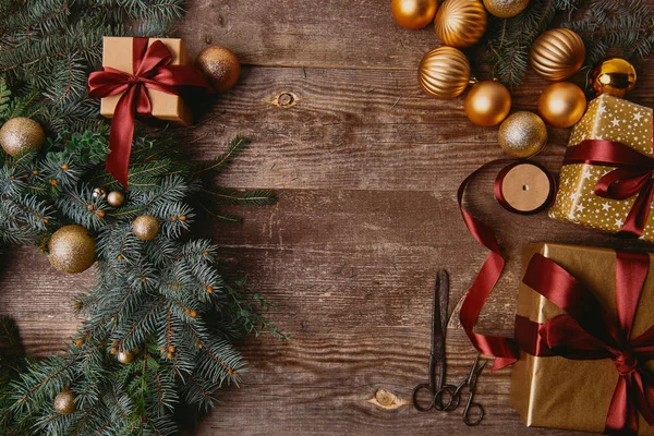 Vista elevada de cajas de regalo de Navidad, corona de abeto, carrete de cinta y tijeras en mesa de madera - foto de stock