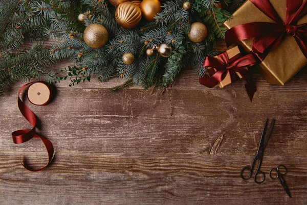 Top view of Christmas gift boxes, fir wreath, ribbon spool and scissors on wooden table — Stock Photo