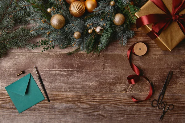 Vista superior de la caja de regalo de Navidad, corona de abeto, carrete de cinta y sobre en la mesa de madera — Stock Photo