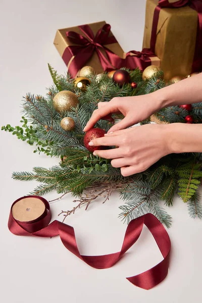 Imagen recortada de la mujer poniendo juguetes en la corona de abeto de Navidad aislado en blanco - foto de stock