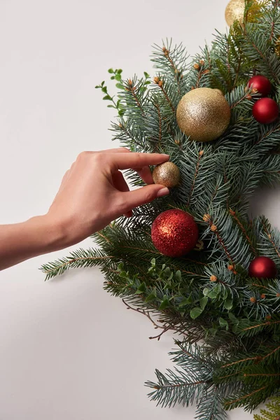 Imagen recortada de la mujer poniendo pequeña chuchería en la corona de abeto de Navidad aislado en blanco - foto de stock