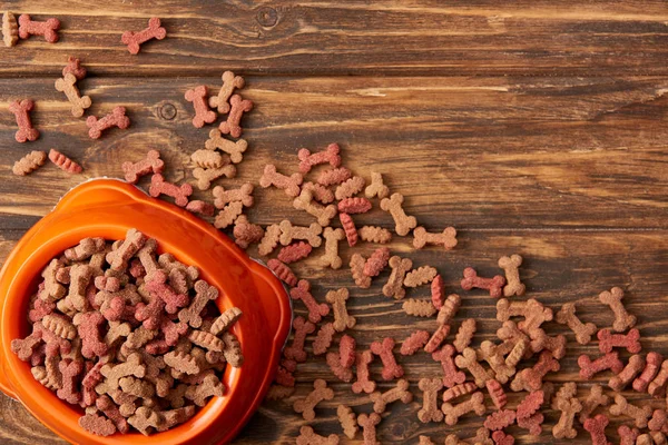 Vista de cima de tigela de plástico com pilha de comida de cão no fundo de madeira — Fotografia de Stock