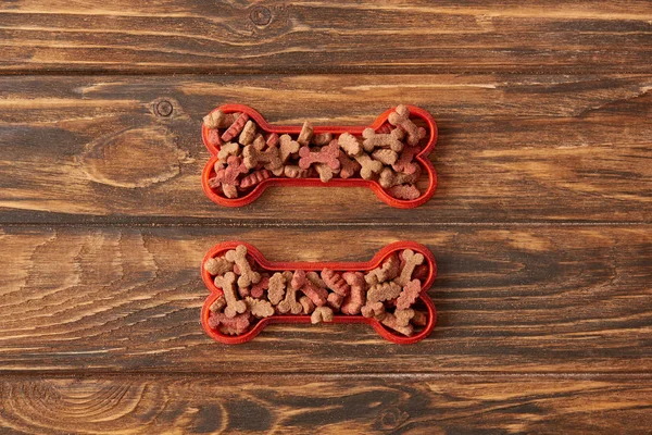 Vista superior de dos huesos de plástico llenos de comida para perros sobre fondo de madera - foto de stock