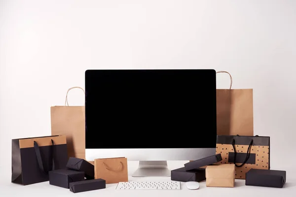 Computer with blank screen with shopping bags and boxes on white surface, black friday concept — Stock Photo