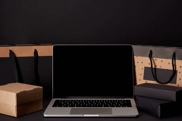 Laptop with blank screen with shopping bags and boxes on black surface, black friday concept — Stock Photo