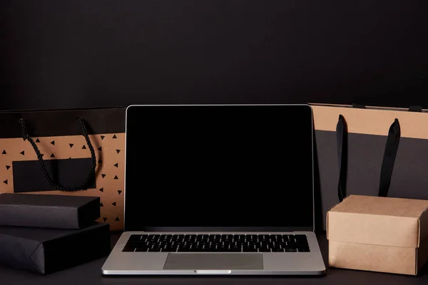 Primo piano del computer portatile con schermo bianco con borse della spesa e scatole sulla superficie nera, concetto di venerdì nero — Foto stock