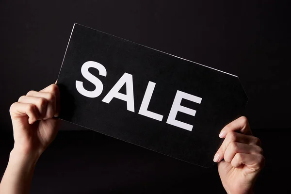 Cropped shot of woman holding banner with sale sign isolated on black, black friday concept — Stock Photo