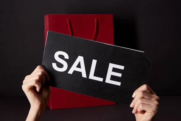 Abgeschnittene Aufnahme einer Frau mit Banner mit Verkaufsaufschrift vor roter Einkaufstasche, Black-Friday-Konzept — Stockfoto