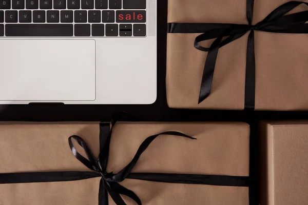 Top view of craft wrapped gift boxes and laptop with black friday button on black surface — Stock Photo