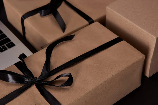 Craft wrapped gift boxes with laptop on black surface, black friday concept — Stock Photo