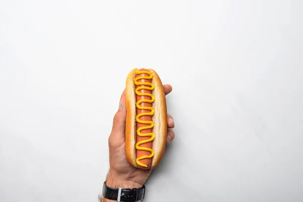 Colpo ritagliato di uomo che tiene gustoso hot dog versato con senape sulla superficie di marmo bianco — Foto stock