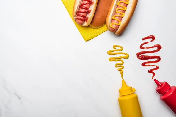 Vista superior de deliciosos perros calientes con mostaza y ketchup en la superficie de mármol blanco - foto de stock