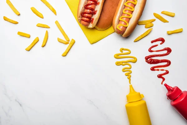 Vista superior de perros calientes con mostaza y ketchup en la superficie de mármol blanco - foto de stock