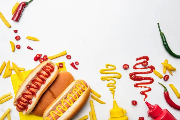 Vista superior de deliciosos hot dogs y papas fritas con mostaza y ketchup en la superficie blanca - foto de stock