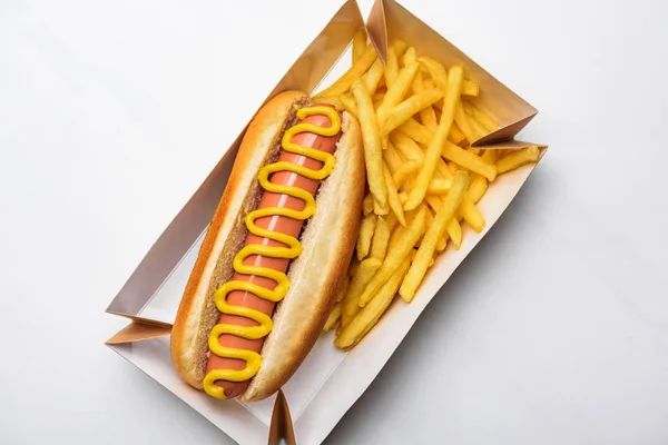 Top view of tasty hot dog with fries in cardboard tray on white — Stock Photo