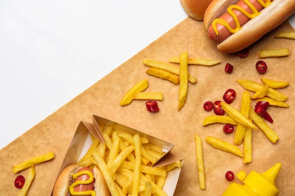 Vista superior de sabrosas papas fritas con perritos calientes en papel pergamino aislado en blanco - foto de stock