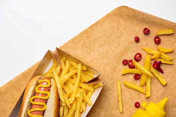 Vista superior de sabroso perrito caliente con papas fritas en papel pergamino aislado en blanco - foto de stock