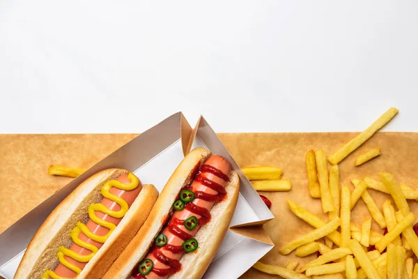Top view of spicy hot dogs with french fries on parchment paper isolated on white — Stock Photo