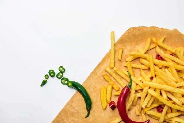 Top view of french fries with spicy peppers on parchment paper isolated on white — Stock Photo