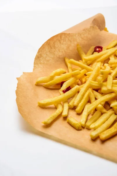 Delicious french fries with spicy peppers on parchment paper on white — Stock Photo