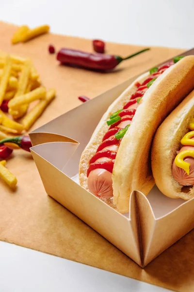 Close-up shot of hot dogs in cardboard tray with french fries on parchment paper — Stock Photo