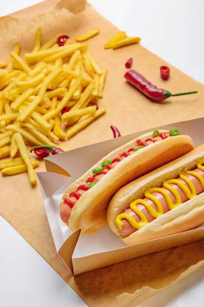 Primer plano de deliciosos hot dogs con papas fritas en papel pergamino - foto de stock