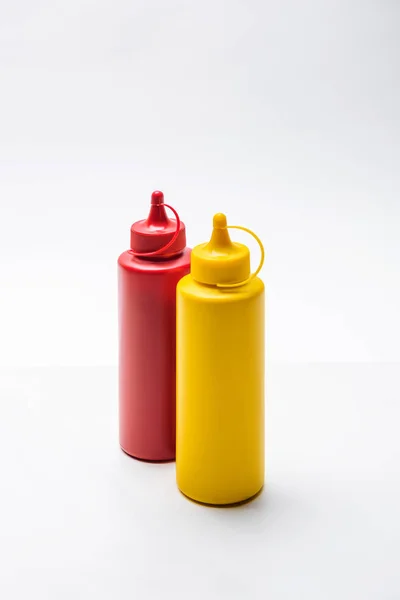 Primer plano de botellas de ketchup y mostaza sobre mesa blanca - foto de stock