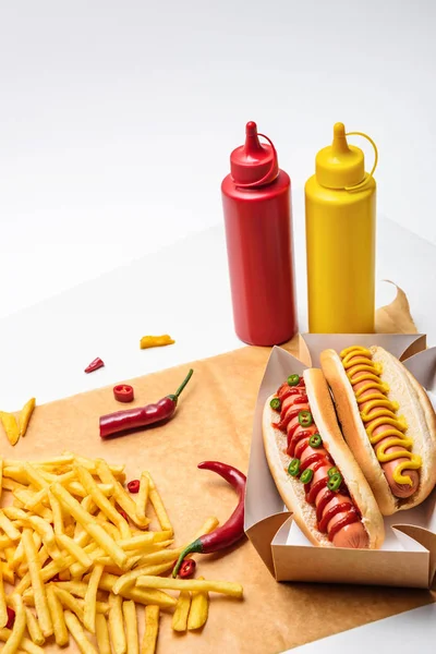 Nahaufnahme von köstlichen Hot Dogs mit Senf und Ketchup auf Papier mit Pommes auf Weiß — Stockfoto