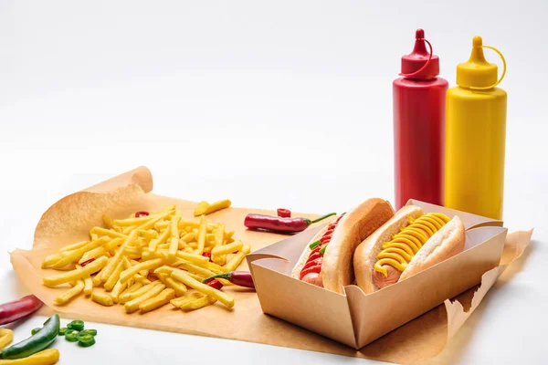 Tiro de close-up de cachorros-quentes saborosos com mostarda e ketchup em papel com batatas fritas em branco — Fotografia de Stock