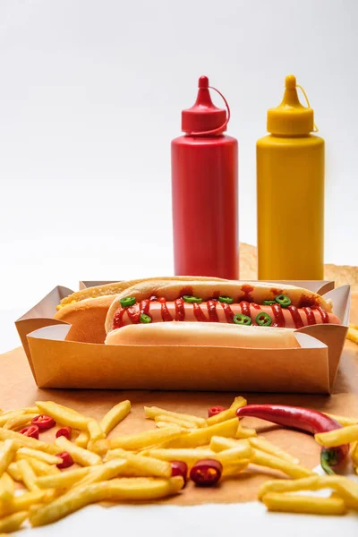 Close-up shot of delicious hot dogs with french fries, mustard and ketchup on paper on white surface — Stock Photo