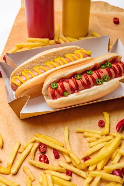 Primer plano de sabrosos perritos calientes con papas fritas en papel sobre la superficie blanca - foto de stock