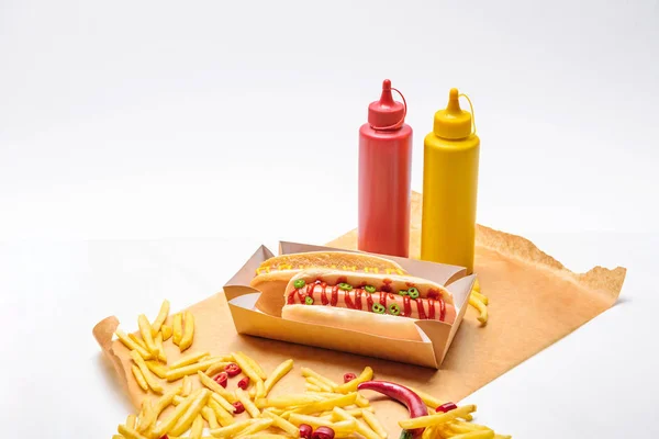 Primer plano de hot dogs con papas fritas, mostaza y ketchup sobre papel sobre superficie blanca - foto de stock