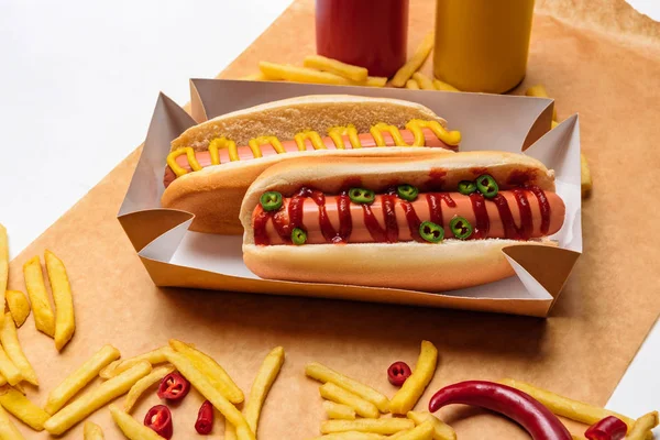 Tiro close-up de cachorros-quentes com batatas fritas em papel na superfície branca — Fotografia de Stock