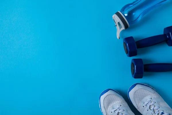 Vista elevada de halteres, tênis e garrafa esporte com água isolada em azul — Fotografia de Stock