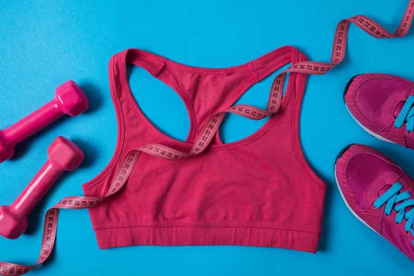 Top view of pink dumbbells, measuring tape, sports bra and sneakers isolated on blue — Stock Photo
