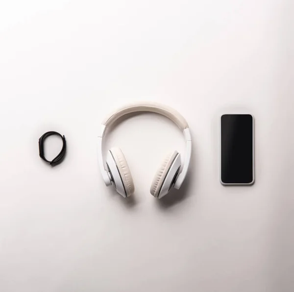 Top view of fitness tracker, headphones and smartphone with blank screen placed in row isolated on white, minimalistic concept — Stock Photo