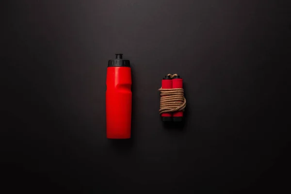 Plano con botella de deporte rojo y cuerda de salto aislado en negro, concepto minimalista - foto de stock