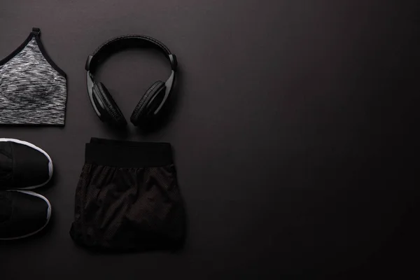 Vista dall'alto di abbigliamento sportivo organizzato e cuffie isolate su nero, concetto minimalista — Foto stock