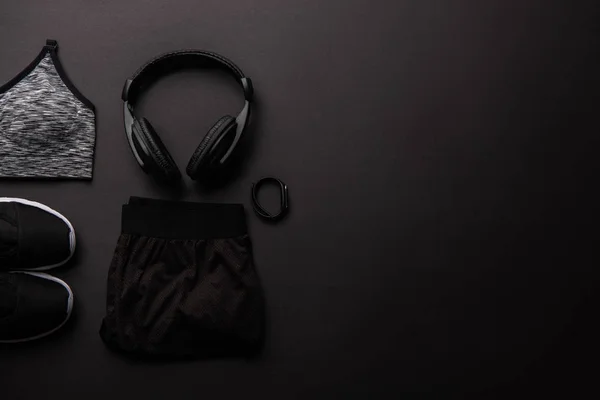 Вид зверху на організований спортивний одяг, навушники та трекер фітнесу ізольовані на чорному — стокове фото
