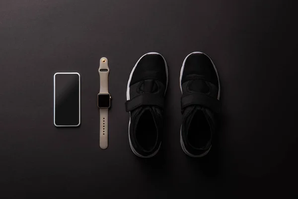 Elevated view of arranged smartphone with blank screen, smartwatch and sneakers isolated on black — Stock Photo