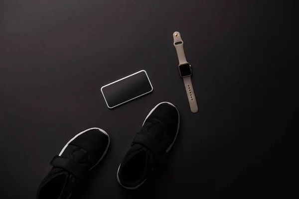 Vue de dessus de smartphone, smartwatch et sneakers isolés sur noir — Photo de stock