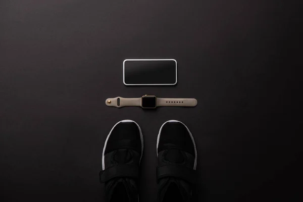 Plano con smartphone arreglado, smartwatch y zapatillas aisladas en negro, concepto minimalista - foto de stock