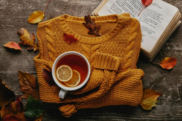 Plat posé avec des feuilles tombées, tasse de thé avec des morceaux de citron, livre et pull orange sur le dessus de table en bois — Photo de stock