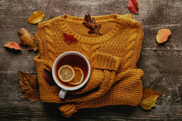 Plat posé avec des feuilles tombées, tasse de thé avec des morceaux de citron et pull orange sur le dessus de table en bois — Photo de stock