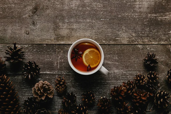 Top view of cup of hot tea and pine cones on wooden tabletop — Stock Photo